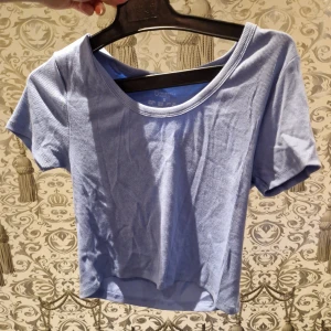 Ljusblå ribbad topp från Primark - Säljer en ljusblå ribbad topp från Primark med korta ärmar och rund halsringning. Toppen är croppad och har en enkel, stilren design som passar perfekt till jeans eller kjol. Materialet är mjukt och stretchigt för en bekväm passform.