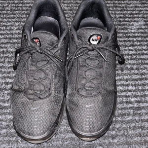 Nike Air Max svarta sneakers - Svarta Nike Air Max sneakers med mesh-ovandel och klassisk snörning. Snygg design med synliga luftbubblor i sulan och diskreta röda detaljer på undersidan. Skorna har rund tå och platt sula, perfekt för dig som gillar sportig och stilren look.