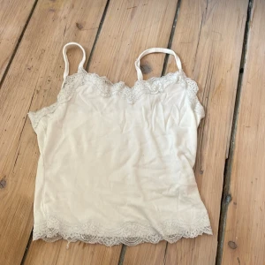 Beige ribbad linnetopp med spets - Supersöt beige linnetopp med tunna axelband och ribbad struktur. Toppen har fina spetsdetaljer längs både ringning och nederkant som ger en romantisk vibe. Perfekt att styla med jeans eller kjol för en chill look.
