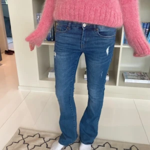 Blå bootcut jeans med slitningar - Snygga blå jeans med bootcut passform med slitningar framtill. Jeansen har klassiska fem fickor, normalhög midja och stängs med dragkedja och knapp. Materialet är jeans med en skön stretch som gör dem bekväma hela dagen.