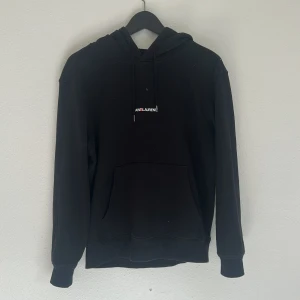Svart Saint Laurent hoodie med logga - Svart hoodie från Saint Laurent med vit och röd logga på bröstet. Klassisk modell med huva, snörning och stor magficka. Tillverkad i mjuk bomull och har långa ärmar. Perfekt för dig som gillar stilrena och exklusiva plagg.