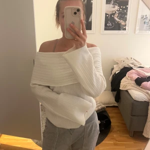 Vit offshoulder stickad tröja - Säljer en vit stickad tröja med bred offshoulder-krage och långa ärmar. Tröjan har ribbad struktur och sitter snyggt över axlarna. Perfekt för dig som gillar en stilren och trendig look.