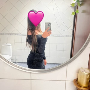 Svart glittrig offshoulder klänning - Säljer en svart glittrig klänning med offshoulder-modell och lång ärm. Klänningen är tight och lång, med en snygg figurnära passform och diskret glans i tyget. Perfekt för dig som vill sticka ut med en elegant och trendig look.