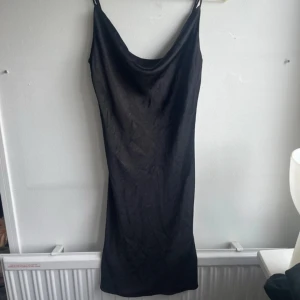 Svart kort satin klänning  - Svart kort drappererad satin klänning från Gina 