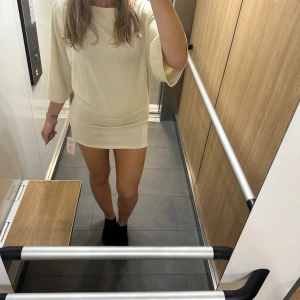 Beige ponchoklänning från Nelly - Superfin beige ponchoklänning från Nelly i stickad bomullsmix. Modellen är kort med lös passform upptill, trekvartsärmar och markerad midja. Perfekt för dig som gillar en enkel men trendig look.