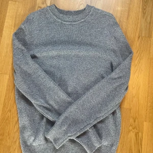 Grå stickad tröja från H&M - Snygg gråmelerad stickad tröja från H&M i regular fit. Tröjan har rund hals, långa ärmar och ribbade muddar vid hals, ärmslut och nederkant. Perfekt för dig som gillar enkel och stilren look med lite struktur i materialet.
