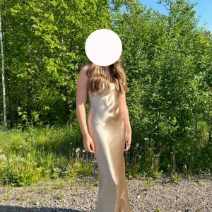 Champagnefärgad långklänning i satin - Säljer min balklänning i guld/champagnefärgad satin. Klänningen har en figurnära passform och en snygg öppen rygg. Jag är ungefär 174cm lång, klänningen är använd 2 gånger! Nypris 900kr!