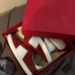 Valentino flycrews - Säljer ett par snygga Valentino Garavani sneakers i rött och vitt med röda skosnören. Skorna har en klassisk låg profil och är tillverkade i mocka och skinn. Kommer i originalkartong och har en cool kontrast mellan färgerna.