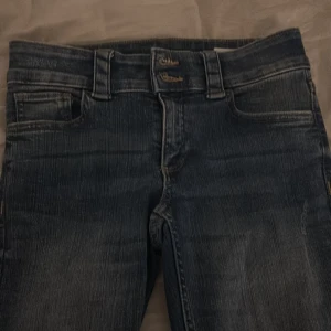 Bootcut jeans - Mörkblå bootcut jeans med snygg slitning och dubbla knappar i midjan. Klassiska femficksdetaljer med bakfickor som har lock och silverfärgade knappar. Jeansen har breda benslut och markerade sömmar för en cool look.