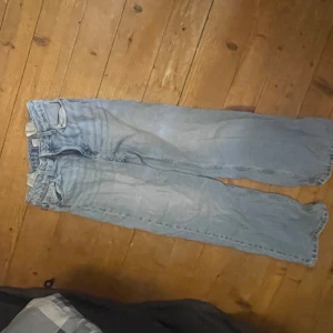 Ljusblå wide jeans med råa kanter - Säljer ett par ljusblå jeans med breda ben och råa, avklippta benslut. Klassisk femficksmodell med normal passform och hög midja. Jeansen har en avslappnad vibe och är perfekta för dig som gillar en loose och trendig stil.