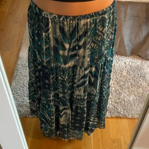 Mönstrad långkjol i blått och beige - Säljer en flowy långkjol med elastisk midja och coolt mönster i blått, beige och grönt. Kjolen har flera lager och ett unikt print som ger boho-vibes. Perfekt för dig som gillar att sticka ut med färg och mönster. Har aldrig använt då den är för kort för mig som är 176💞💞