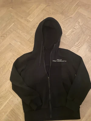 Svart Peak Performance hoodie med dragkedja - Svart hoodie från Peak performance med zip. Funkar både till träning och vardaglig användning. Använd men fortfarande i mycket bra skick