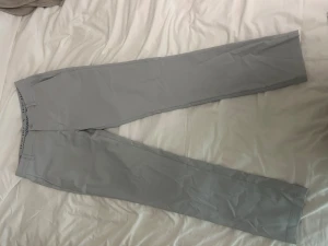 Ljusgrå kostymbyxor från Puma - Snygga ljusgrå golfbyxor från Puma med klassisk rak passform och diskreta fickor bak. Byxorna har bälteshällor och är tillverkade i ett mjukt och slitstarkt material som ger en clean look. Perfekta för dig som gillar stilrena och sportiga vibes.