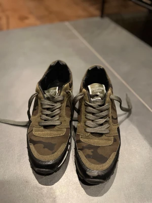 Valentino Rockrunner sneakers camouflage - Snygga Valentino Rockrunner sneakers med grön och brun camouflage-mönster, svarta och vita detaljer samt coola nitar runt hälen och sulan. Perfa för vintern för att hålla sig varm ❄️🌨️ Box medföljer ej!