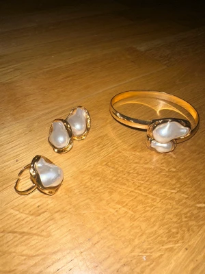 Guldarmband och örhängen med pärldetaljer - Säljer ett set med armband och örhängen i guldton med stora, oregelbundna pärlliknande detaljer. Snyggt och unikt smyckeset som verkligen sticker ut och ger en lyxig känsla. Perfekt för dig som gillar statement-accessoarer.