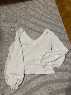 Vit blus med v-ringning och puffärm - Säljer en vit blus med v-ringning och långa puffärmar. Blusen har ett subtilt mönster i tyget och breda muddar vid ärmsluten. Perfekt för dig som gillar en stilren och trendig look. 