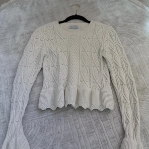 Vit stickad tröja Holly & Whyte XS - Supersöt vit stickad tröja från Holly & Whyte med snyggt strukturmönster och volangkant nedtill. Tröjan har långärmade ärmar och rund halsringning. Perfekt för dig som gillar detaljer och vill ha en mysig look.