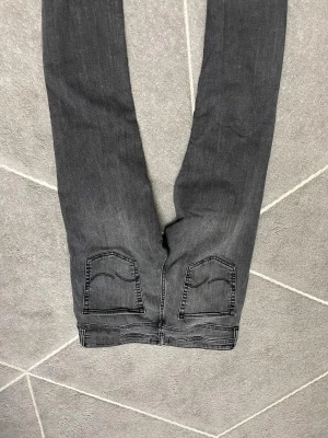 Jack&Jones jeans  i storlek 32/34 - Snygga grå jeansbyxor med klassiska femficksdetaljer och svarta sömmar. Modellen har raka ben och subtila slitningar för en cool look. Passar dig som gillar en enkel och stilren stil. Materialet är mjukt ock skönt