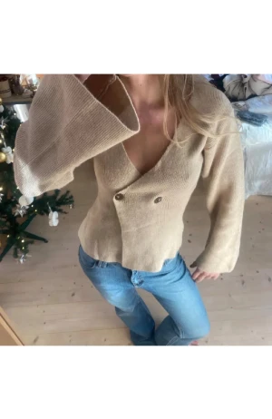 Beige stickad kofta med v-ringning - Snygg beige stickad kofta med breda långa ärmar och djup v-ringning. Koftan har två knappar framtill och är figurnära med en loose passform. Använd 1 gång och köpt på plick. Lånade bilder❤️