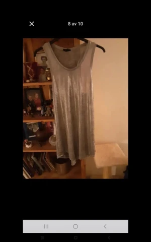 Silvrig ärmlös kortklänning - Snygg silvrig kortklänning med rund halsringning och ärmlös design. Klänningen har en glansig finish som ger en festlig känsla och är tillverkad i ett mjukt material som faller fint. Perfekt för dig som vill sticka ut med en enkel men cool look.