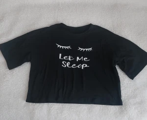 Svart t-shirt Let Me Sleep - Svart  t-shirt med vitt tryck av stängda ögonfransar och texten 'Let Me Sleep' på bröstet. T-shirten har korta ärmar och är tillverkad i en mjuk blandning av bomull och polyester. Perfekt för en chill och avslappnad stil.
