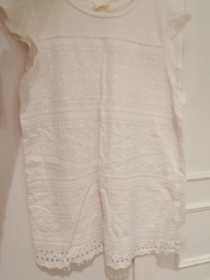 Vit broderad blus   - Superfin blus från H&M L.O.G.G. i bomull med broderade detaljer och volang vid ärmarna. Blusen har hålmönster och spetskant nertill, perfekt för en ljus och fräsch look. Rak passform och ärmlös design. Den är endast använt få gånger, sedan stått i garderoben. 😊