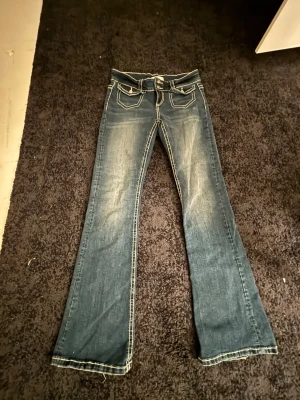 Blå bootcut jeans med kontrastsömmar - Snygga blå bootcut jeans från Perfect Jeans med markerade vita kontrastsömmar och dubbla knappar i midjan. Framtill finns fickor med lock och bakfickorna har coolt broderade detaljer. Jeansen har låg midja och är tillverkade i klassiskt denimtyg. Endast använda två gånger. Storlek M. Hör av dig via e-mejl eller telefonnummer då jag inte kan ta emot Swish på detta nummer e-mejl emli.com@icloud.com mobil-0728875624 mvh Emilia/marina😊