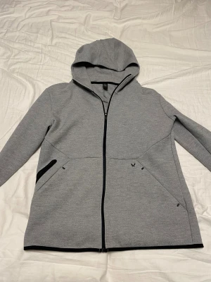 Grå hoodie från SOC med dragkedja - Snygg grå hoodie från SOC i storlek M. Tröjan har hel dragkedja framtill, huva och svarta detaljer vid fickorna. Perfekt för chill eller träning, med långärmad design och mjukt material som känns skönt mot huden.