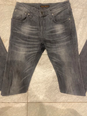 Grå jeans från Nudie Jeans Co W27 L32 - Snygga grå jeans från Nudie Jeans Co med coola slitningar och klassisk femficksdesign. Jeansen har en rak passform och är tillverkade i mjukt jeanstyg. Perfekt för dig som gillar en avslappnad och stilren look.