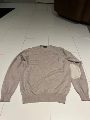 Beige stickad tröja Stenströms - Snygg beige stickad tröja från Stenströms med rund hals och ribbade muddar. Tröjan har lång ärm och coola ljusa armbågslappar som ger en extra touch. Perfekt för dig som gillar stilren och klassisk look.