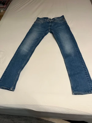 Blå Replay jeans straight fit - Säljer ett par klassiska blå jeans från Replay med snyggt slitna detaljer och raka ben. Jeansen har fem fickor, normal passform och tydlig Replay-logga på bakfickan. Perfekta för dig som gillar en tidlös och avslappnad stil.