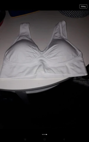 Vit ärmlös linnetopp - Säljer en vit, enkel och bekväm linnetopp med breda axelband och sömlös design. Toppen är ärmlös och har en mjuk, stretchig passform som passar perfekt till träning eller som basplagg. Materialet känns mjukt mot huden och ger bra stöd.