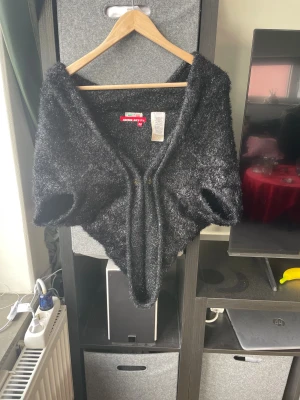 Svart fluffig kofta från Miss Sixty - Unik svart kofta från Miss Sixty i storlek M, tillverkad i Italien. Koftan har en fluffig och glansig yta med en cool asymmetrisk form som ger en edgy vibe. Materialet är en mix av polyamid och angora, vilket gör den supermjuk och skön. Perfekt för dig som gillar statement-plagg.