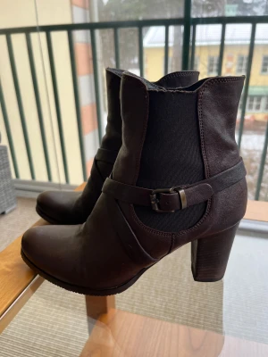 Ankelboots i skinn med klack - Ankelboots med kort skaft och ca 8 cm hög klack. Materialet är skinn. Dragkedja på insidan. Lite stretch på yttersidan. Old Castagno från d’essai. Inköpta på Jerns. Pris 1950kr. Endast använda handfull gånger. Det är storlek 38. Lite smal modell.