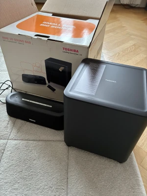 Toshiba Mini 3D Sound Bar med Subwoofer SBM11W - Toshiba Mini 3D Sound Bar med subwoofer SBM11W, Bluetooth, 3D-ljud, kompakt design och två digitala ingångar. Komplett med originalkartong, fjärrkontroll och kablar. Produkten ser välvårdad ut, kartongen har visst yttre slitage men enheten är i fint skick.