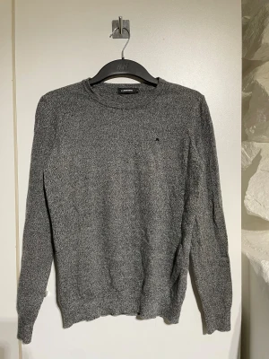 Grå stickad tröja J.Lindeberg - Snygg grå stickad tröja från J.Lindeberg med diskret logga på bröstet. Rund hals och långärmad modell med normal passform. Perfekt för dig som gillar stilrena och enkla plagg med en modern touch. Strlk 158-164 junior storlek M