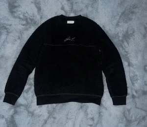 Svart tröja från Pier One - Mysig svart fleece-tröja från Pier One med broderad vit signatur på bröstet. Tröjan har rund hals, ribbade muddar och en loose passform som ger en chill vibe. Perfekt för kalla dagar när du vill vara både bekväm och snygg.