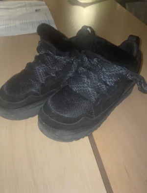 Uggs lowmel  - Säljer ett par svarta sneakers från UGG med grov sula och snörning. Skorna har ett mysigt svart foder i pälsimitation och ovandel i mesh och mocka. Perfekta för dig som vill ha både stil och komfort under kyligare dagar.
