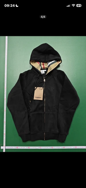 Svart Burberry hoodie med dragkedja - Svart hoodie från Burberry med klassiskt rutigt foder i huvan och guldfärgad dragkedja. 