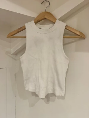 Vit ribbad linnetopp från Kappahl - Säljer en enkel och stilren vit ribbad linnetopp från Kappahl i storlek XS. Toppen är ärmlös med hög halsringning och croppad passform, perfekt till jeans eller kjol. Materialet är mjukt och stretchigt för en bekväm känsla.