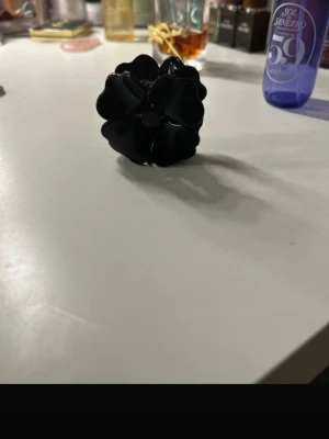 Svart hårklämma i blomform - Snygg svart hårklämma formad som en blomma med glansig finish. Perfekt accessoar för att piffa till frisyren och hålla håret på plats. Klämman har en stilren och enkel design som passar till många olika looks.