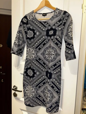 Mönstrad klänning från Bubbleroom - Snygg kort klänning från Bubbleroom med svartvitt paisleyinspirerat mönster. Modellen har trekvartsärm och rund halsringning. Materialet är mjukt och stretchigt, perfekt för dig som gillar bekväma och stilrena plagg.