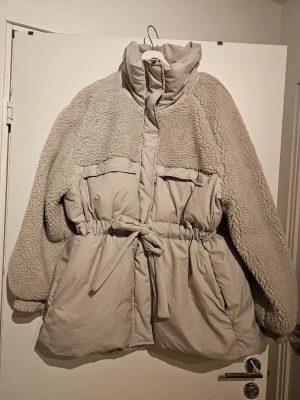Beige teddy- och pufferjacka H&M XL - Säljer en beige teddy- och pufferjacka från H&M i storlek XL. Jackan har hög krage, stora fickor framtill och knytband i midjan. Överdel och ärmar i mjuk teddy, nederdel i vadderad pufferstil. Perfekt för kalla dagar och riktigt snygg oversized look.