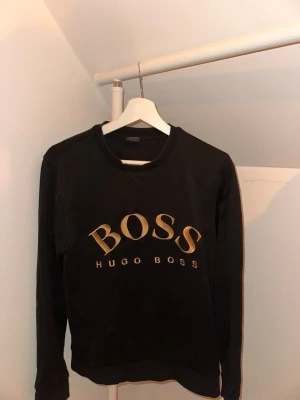 Svart sweatshirt från Hugo Boss - Svart sweatshirt från Hugo Boss med stort guldfärgat BOSS-tryck på bröstet, Skick 10/10         Äkta! 