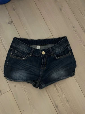 Mörkblå vintage jeansshorts🩷 - Säljer ett par mörkblå lowwaist vintage jeansshorts. Shortsen har guldfärgade detaljer, bälteshällor och en snygg läderpatch bak. Perfekta till sommaren och har en normal passform.🩷