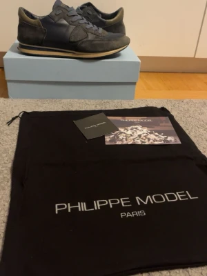 Philippe Model blå sneakers mocka & skinn - Snygga sneakers från Philippe Model i mörkblått med detaljer i mocka och skinn. Skorna har rund tå, platt sula och snörning. Klassisk design med diskret logga på sidan och kontrastfärgad kant på sulan. Perfekta för dig som gillar stilrena och exklusiva sneakers.