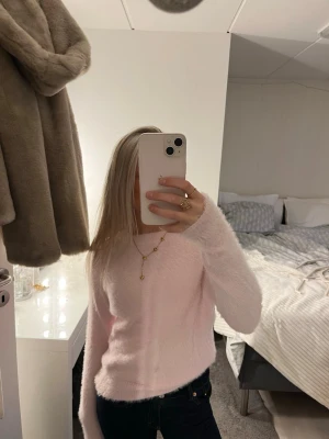 Ljusrosa fluffig stickad tröja - Supermjuk och fluffig ljusrosa stickad tröja med lång ärm. Perfekt för dig som vill ha en mysig och enkel look. Tröjan har en klassisk rund halsringning och är lätt att matcha med jeans eller kjol.