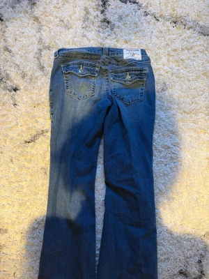 MörkBlå True Religion jeans bootcut 27 - Storlek 27! Säljer ett par klassiska blå jeans från True Religion med ikoniska bakfickor och kontrastsömmar. Modellen har bootcut-ben och normal passform. Jeansen har detaljerade ficklock med knappar och är tillverkade i slitstark denim.