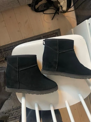 Svarta UGG boots W classic femme moni - Säljer ett par  svarta UGG boots i mjuk mocka med rund tå och plattå. Skorna har en låg siluett och är fodrade för extra värme. Perfekta för kyliga dagar och riktigt sköna att ha på sig. Passar till det mesta och är superlätta att dra på.