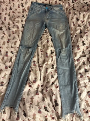 Replay ljusblå skinny jeans med slitningar - Säljer ett par ljusblå skinny jeans från Replay med slitna knän och råa, fransiga benslut. Jeansen har en blå knapp och en liten glittrig detalj vid fickan. Klassisk femficksmodell i stretchigt denimtyg. 25w30L